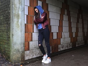 A tired-looking teenage girl wearing a hoodie leans against a wall