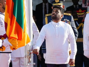 A man in a white shift raises a Sri Lankan flag using a small wheel