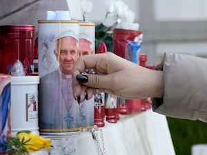 A woman lays a rosary near candles adorned with pictures of Pope Francis