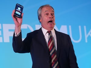 Reform UK leader Nigel Farage holding a phone displaying the number of Reform UK party members while speaking during the Reform UK East of England conference at Chelmsford City Racecourse