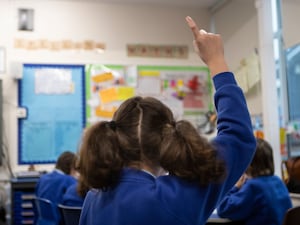 A girl raises her hand in a class with other pupils