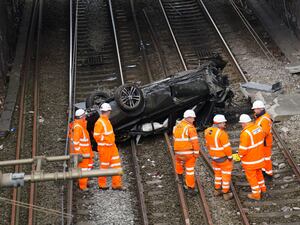 Emergency workers view a car that crashed onto tracks