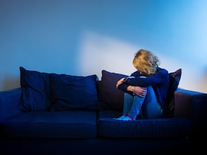 A woman in jeans and a dark top sitting curled up on a blue sofa