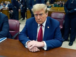 Trump sat at a wooden court table, he wears a blue suit with red tie