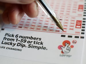 A person holds a pen over a lottery numbers slip