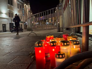 Lit candles stand on a street, with a person in the distance