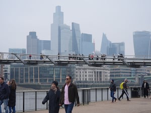 People walk across the Millennium Bridge with the City of London in the background