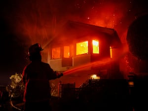 A firefighter, pictured, as a Palisades Fire burns a house in the hill next to the Getty Villa