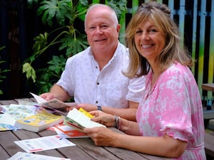 Man and a woman sat by a wooden table outside as they read letters