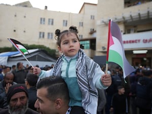 A young girl waving Palestinian flags on shoulders of a man