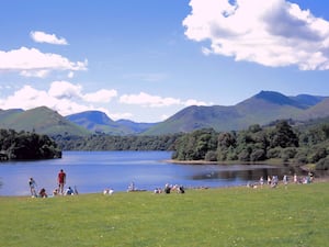 People sit on the grass by Derwent Water with Lake District hills in the background