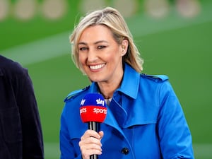 Kelly Cates pictured smiling and holding a microphone as she presents Sky coverage of a Premier League match between Burnley and Manchester City