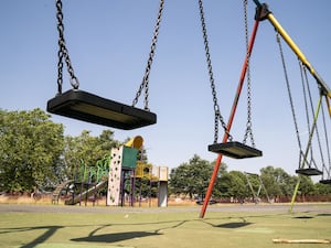 Stock image of a children's playground with swings in the foreground and a slide in the background