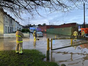 Firefighters stand on a flooded road