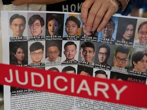 A supporter holds a placard with the photos of some of the 47 pro-democracy defendants outside a court in Hong Kong