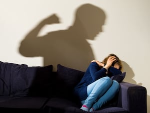 A woman cowering on a sofa, with the shadow on the wall behind her of a man with his fist raised