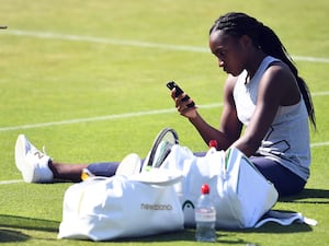 Coco Gauff sitting on a tennis court looking at a phone in her hand