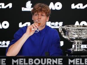 Jannik Sinner drinks champagne as he sits next to the Australian Open trophy