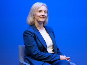 Liz Truss sitting on stage with blue backdrop