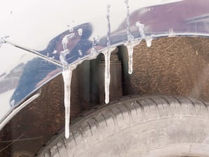 Icicles of water hanging on car above one of its tyres