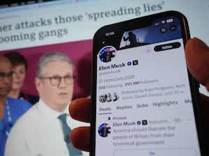 A phone showing Elon Musk's tweets, held in front of an image of Sir Keir Starmer